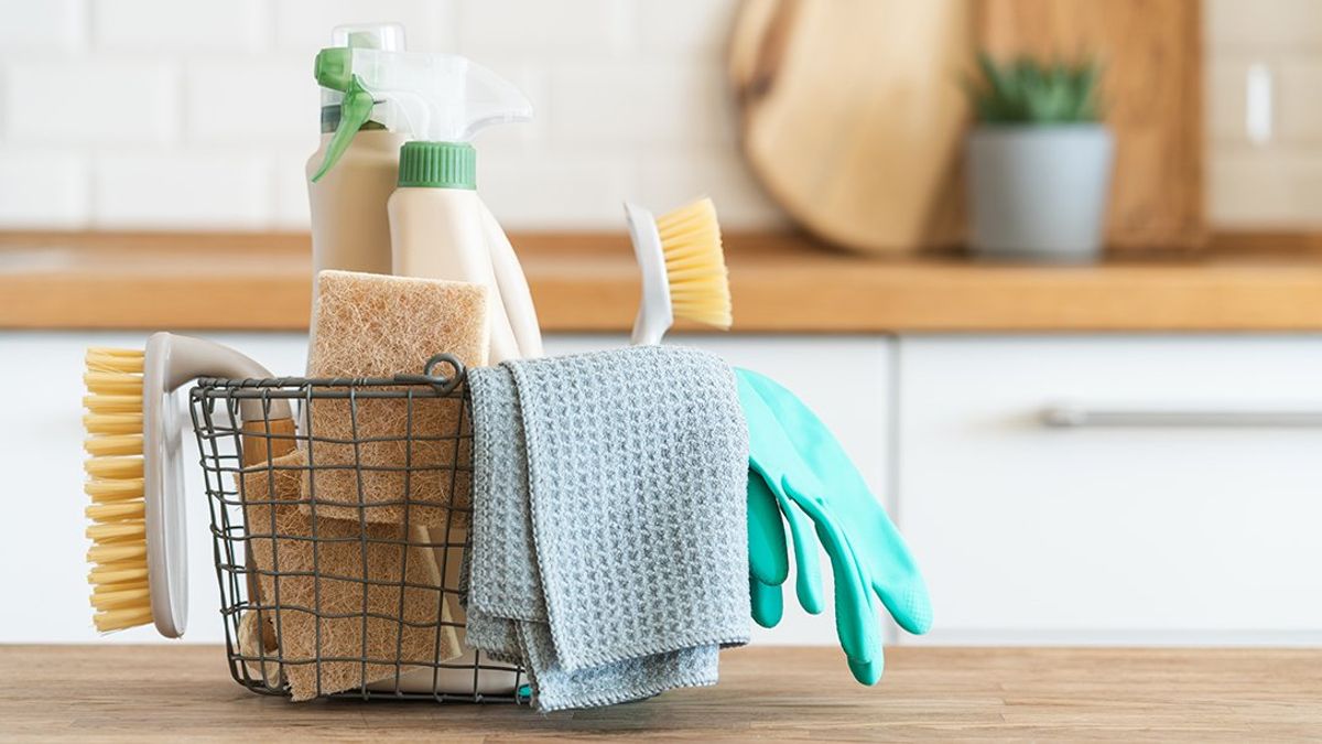 A closeup of a wire basket filled with house cleaning supplies sitting on a kitchen counter.