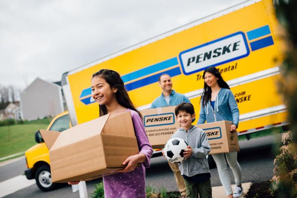 A family carries boxes away from a yellow Penske moving truck.