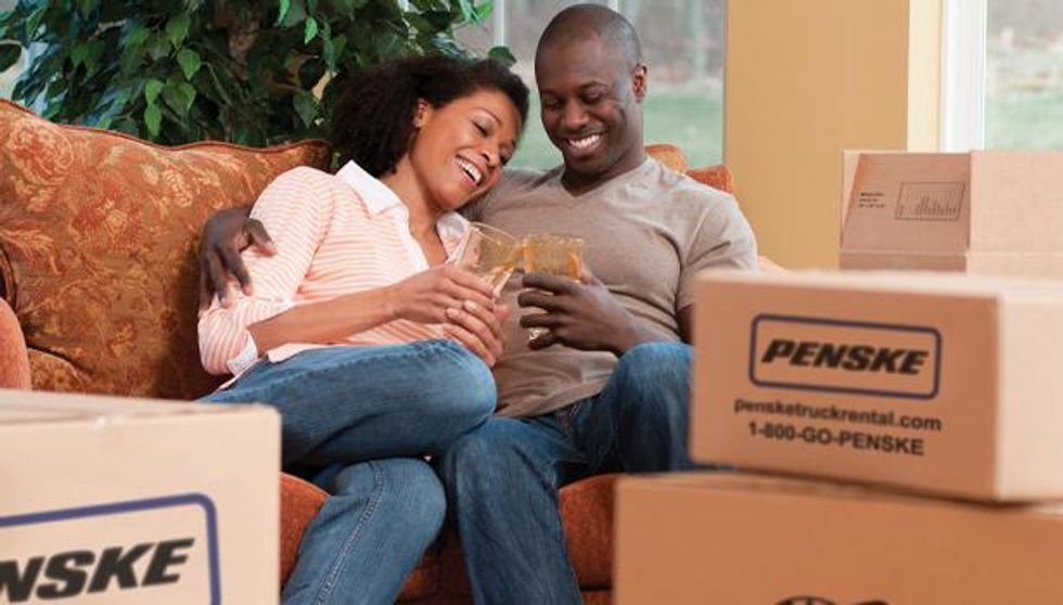 A man and woman sit next to eachother on an orange couch while clinking glasses.