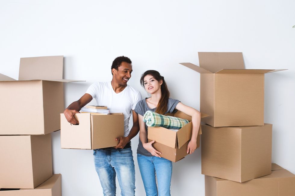 A man and woman stand holding moving boxes, surrounded by more boxes.