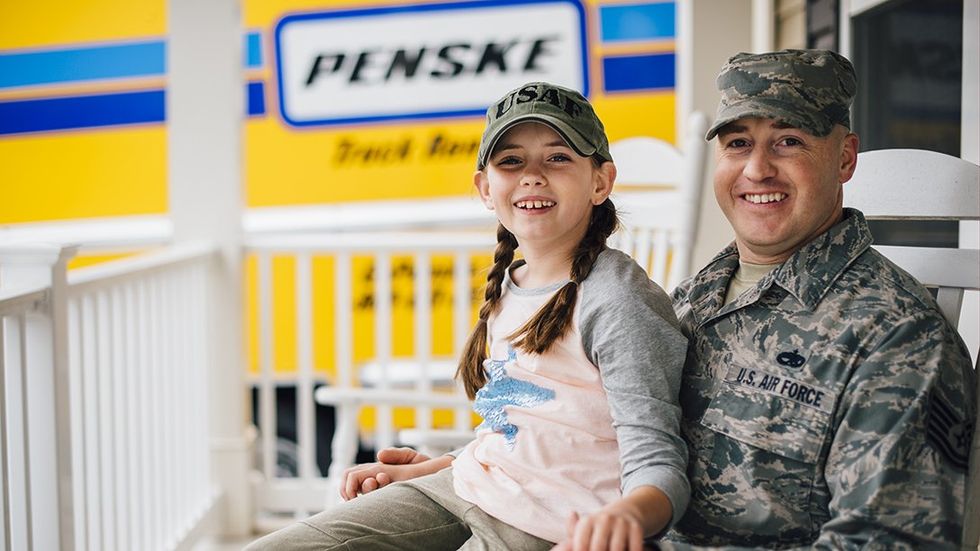 A member of the Air Force sits on a porch with a girl on his lap and a yellow Penske moving truck in the background.