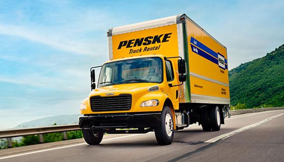 A yellow Penske moving  truck driving on the road.