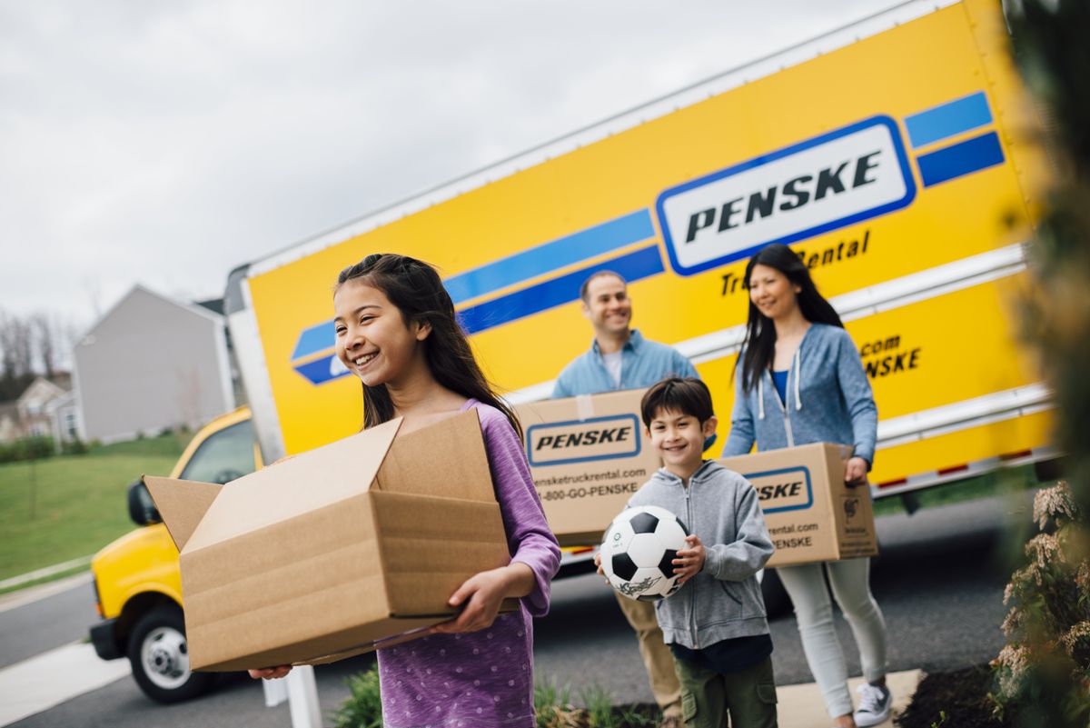 Family walking away from a moving truck carrying boxes.