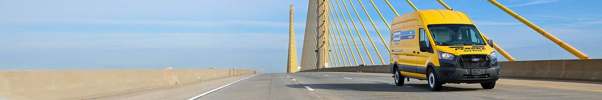 Penske high-roof cargo van driving on a highway crossing a suspension bridge