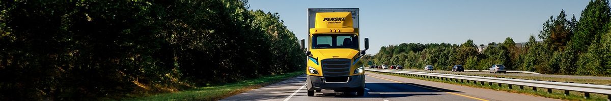 Penske tractor trailer drives on a tree-lined highway