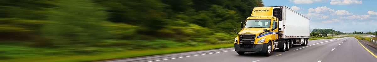 Penske tractor trailer driving on a tree-lined highway