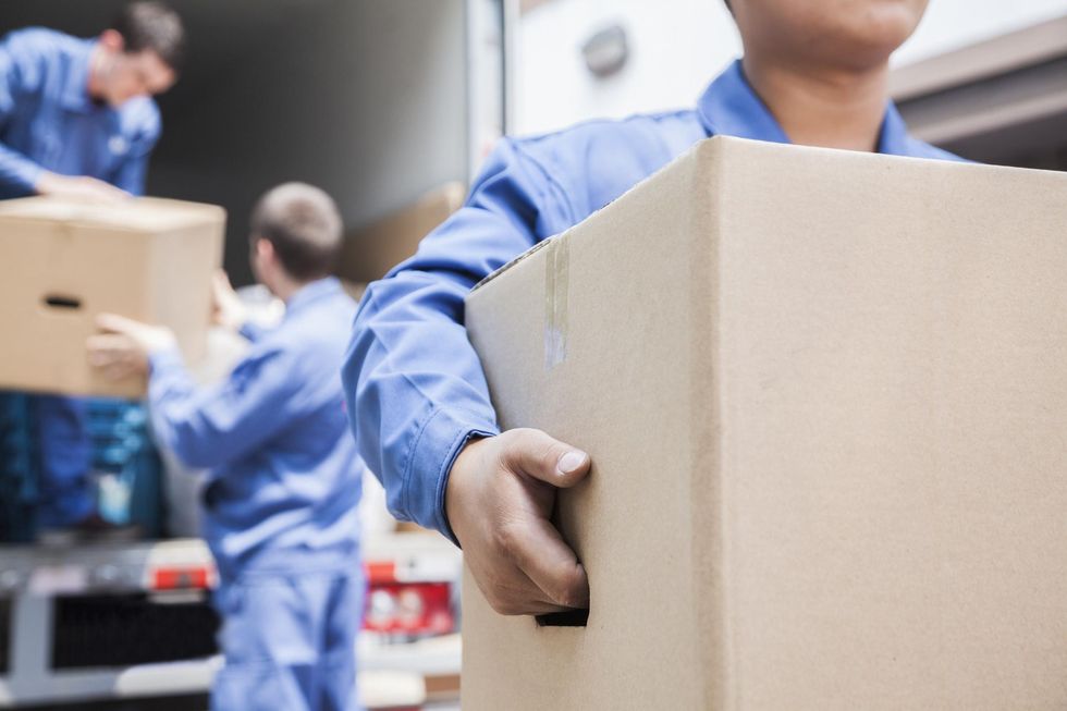 Professional movers in blue jumpsuits move boxes from a moving truck.