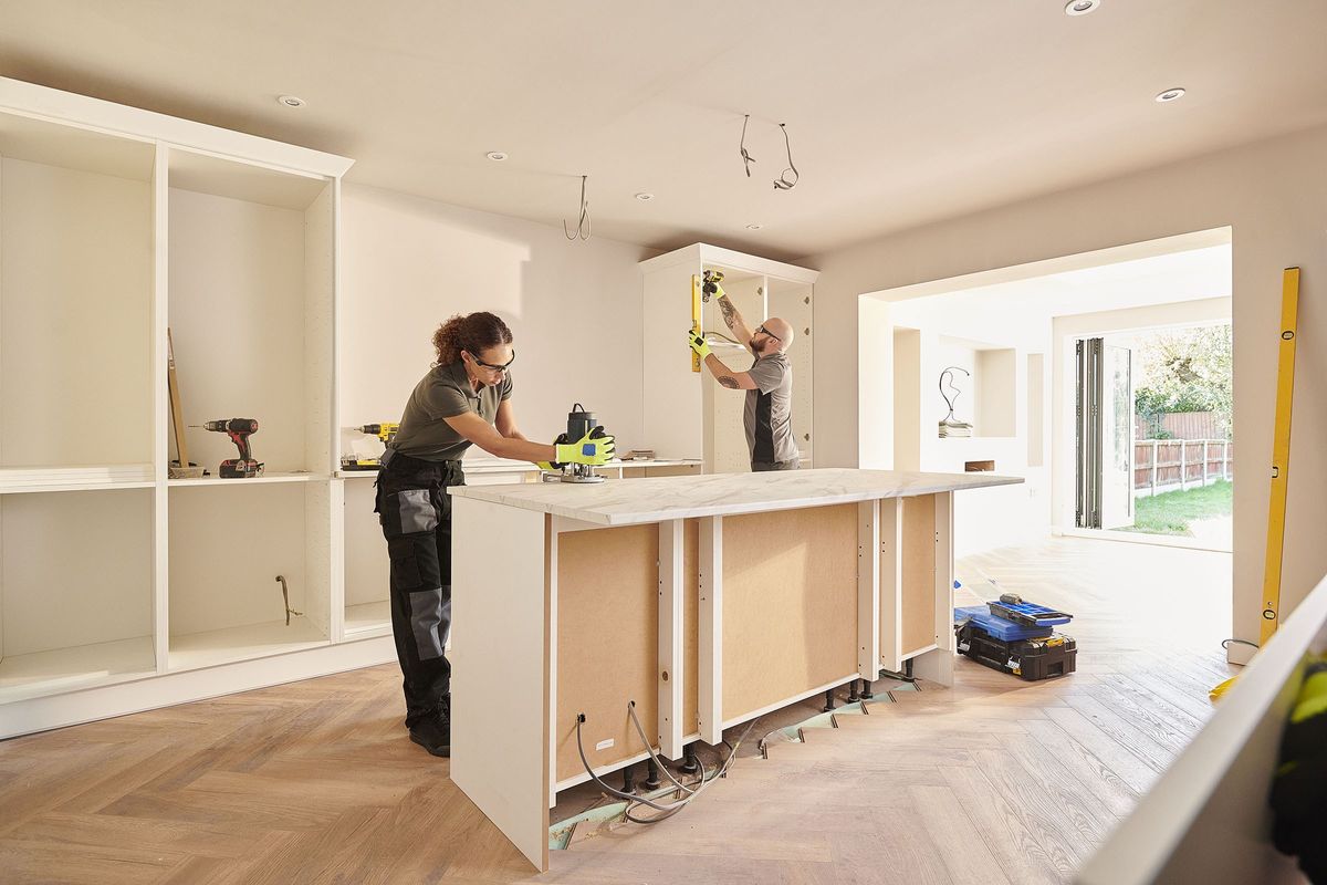 Two tradespeople work on installing a new kitchen.