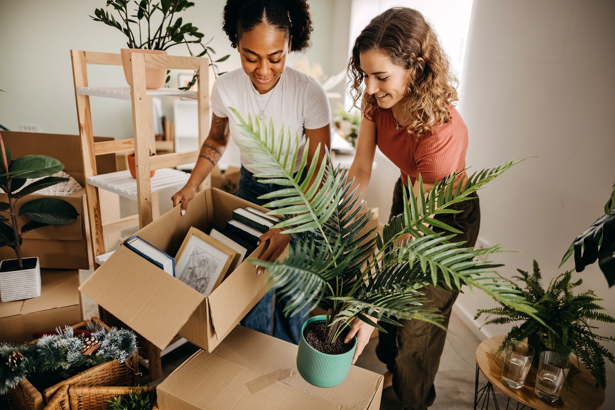 Two women pack up boxes and plants.